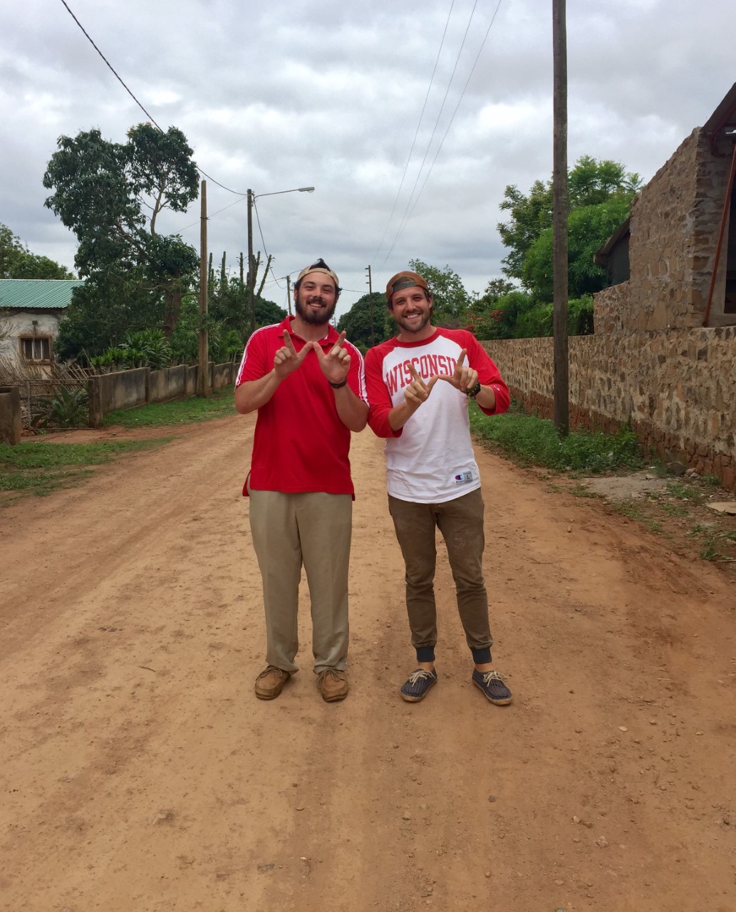 Two Peace Corps volunteers standing together on a dirt road making a W shape with their hands
